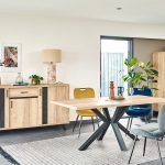 Photo d'une salle à manger avec une collection comprenant une enfilade, une table de repas, des chaises et un meuble de rangement. Les meubles présentent des finitions en chêne naturel style brut industriel et des piétements en métal noir.